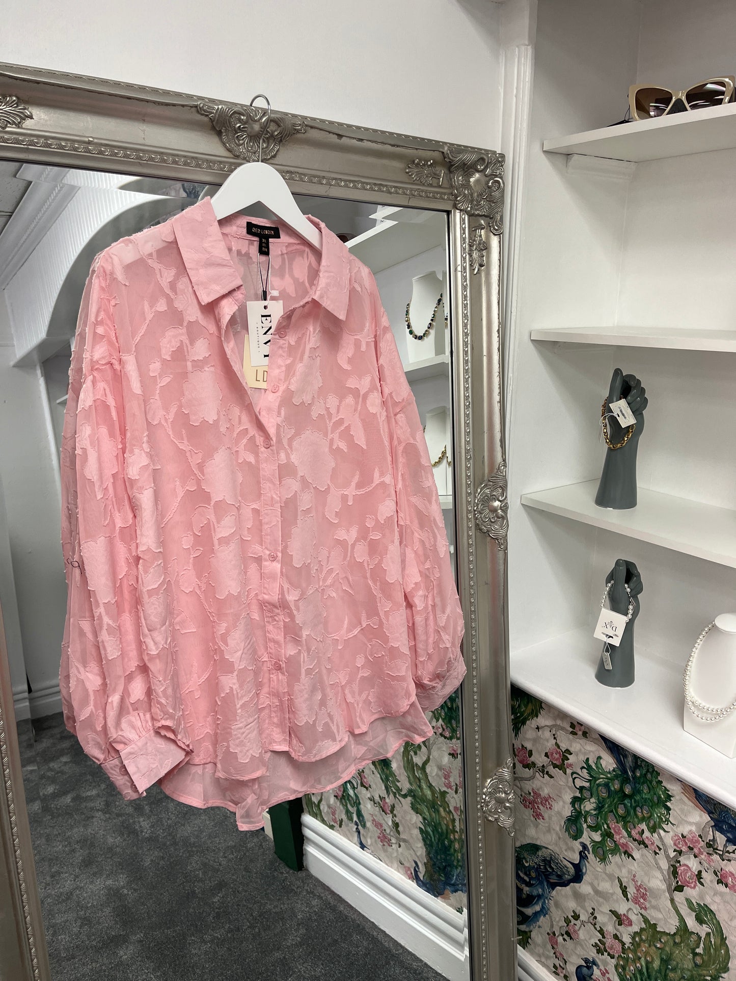 Delicate pink sheer shirt with a floral pattern, crafted from 100% polyester, styled on a model for a breezy, elegant look.